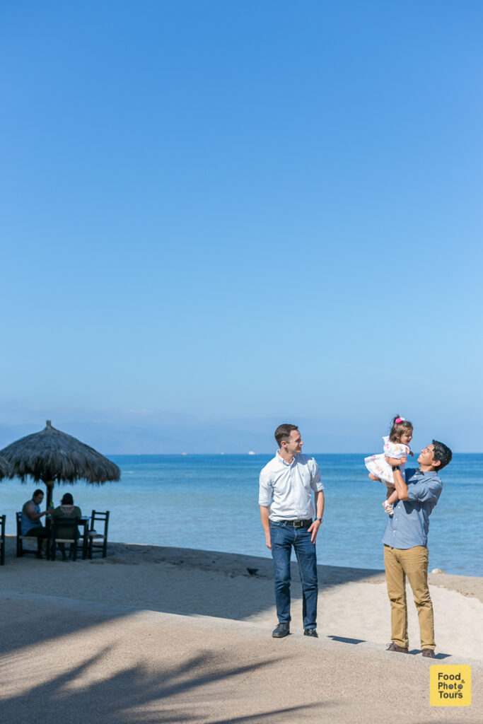 Gay Couple and their toddler daughter with an LGBT Family Photographer in Puerto Vallarta on a photo shoot at the beach+ Vallarta Pride
